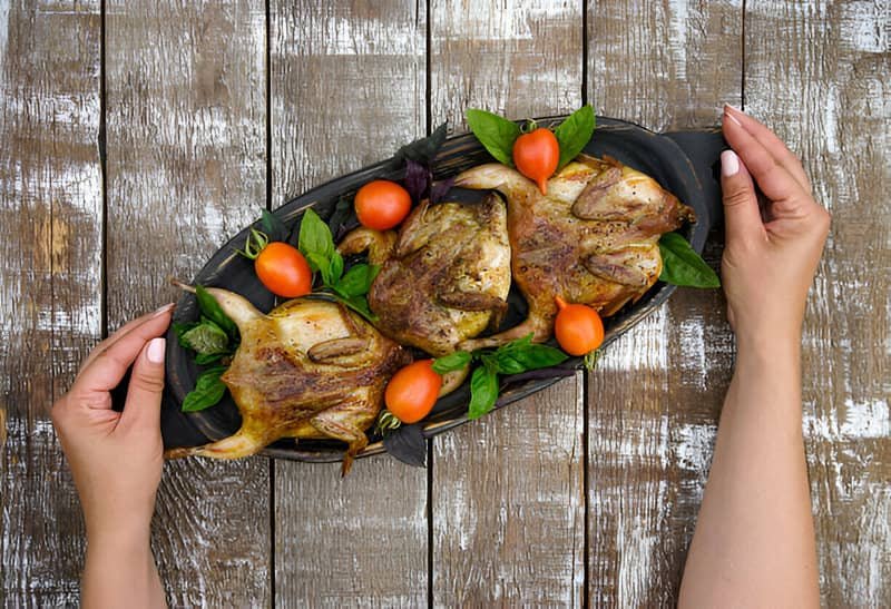 Tres codornices a la brasa en una bandeja negra acompañadas de verduras