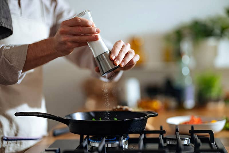 Un cocinero añade sal a lo que está preparando en una sartén