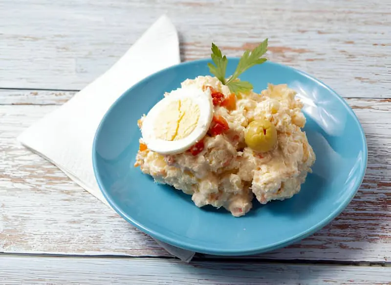 Un plato azul con ensaladilla rusa y una servilleta sobre una mesa de madera