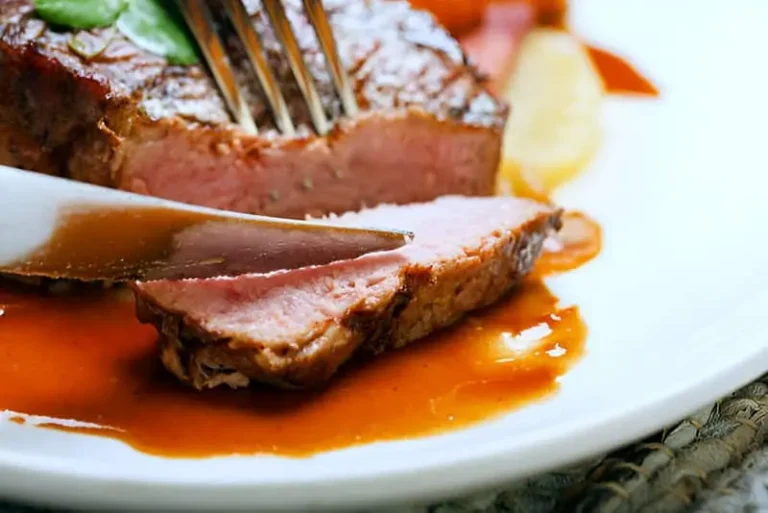 Cortando con un cuchillo y un tenedor un trozo de solomillo de ternera en reducción de vino tinto