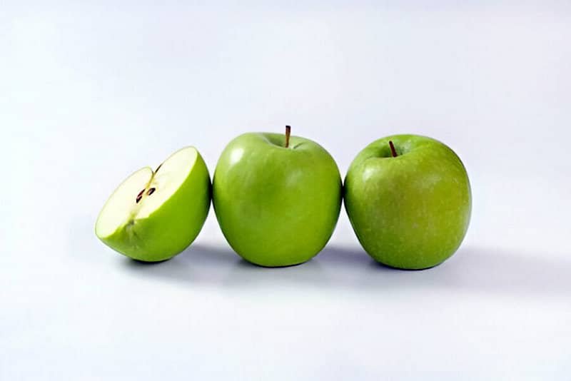 Dos manzanas verdes enteras y una cortada por la mitad sobre un fondo blanco
