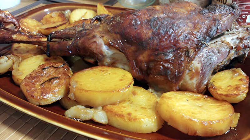 Una bandeja con una pierna de cordero asada y papas panaderas