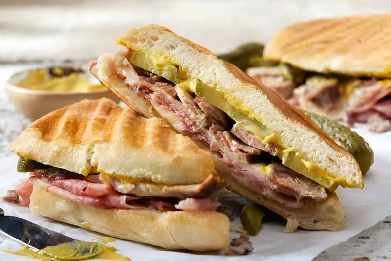 Un sándwich cubano cortado en dos y puesto sobre un plato cuadrado