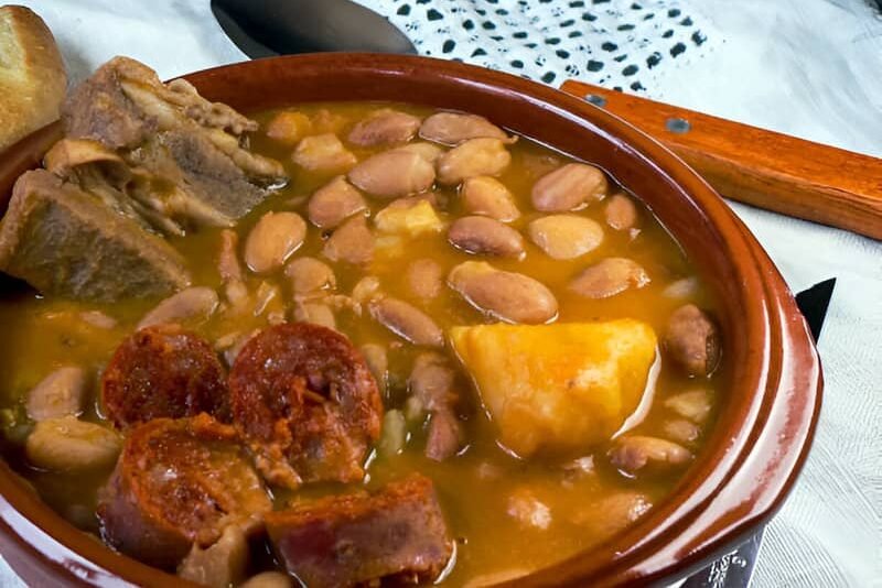Un cuenco de barro sobre un mantel, con Alubias Pintas con Patatas, Costillas de Cerdo y Chorizo