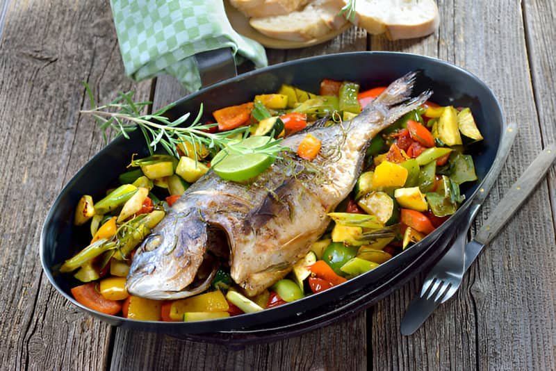 Una bandeja de pescado al horno con verduras