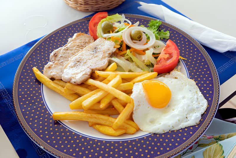 Un plato combinado con patatas fritas, huevo, lomo de cerdo y ensalada