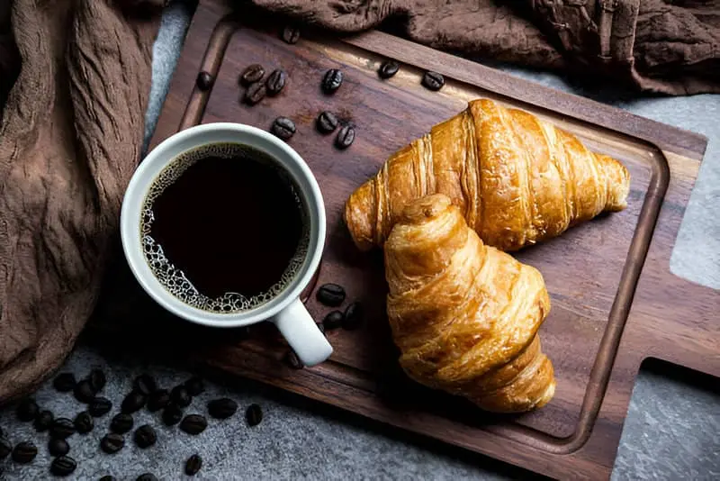 Dos Croissants y una taza de café sobre una tabla de madera
